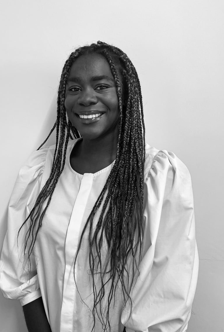 A smiling young Black woman with long braids wearing a white puff-sleeve blouse in a black and white portrait.