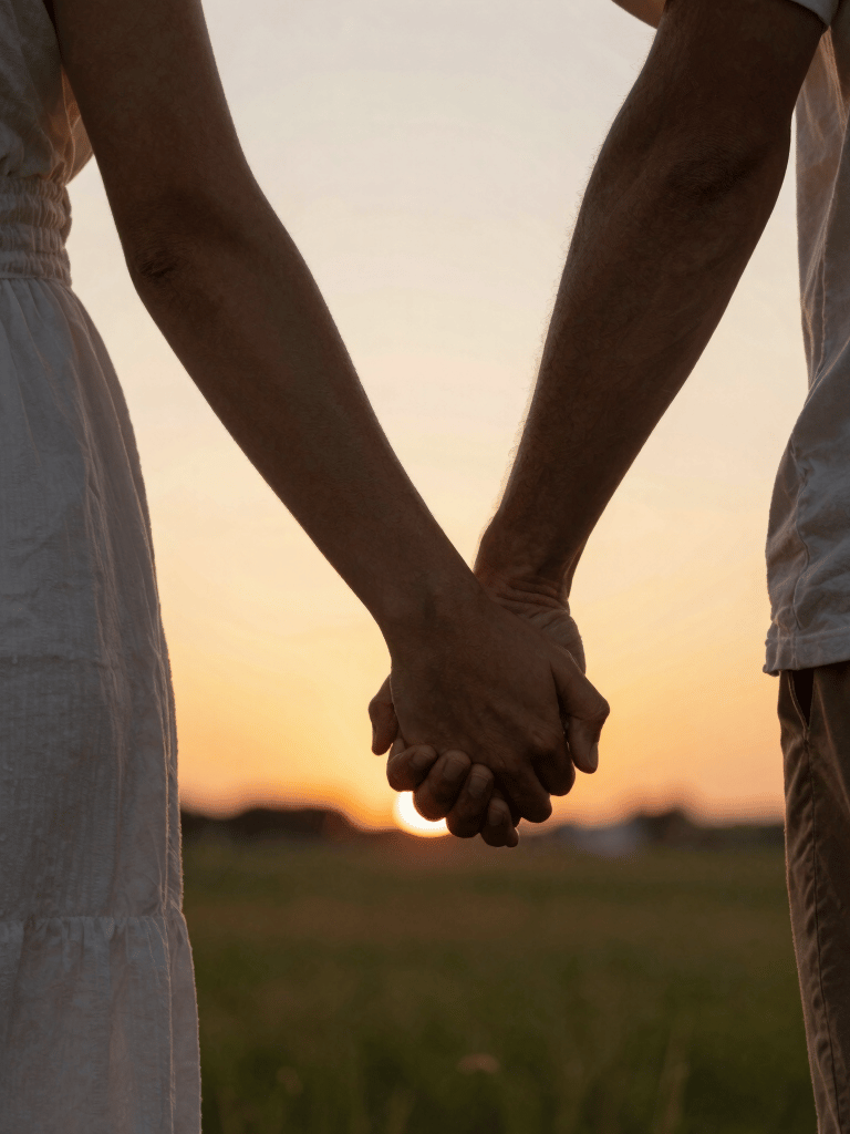 A romantic couple holding hands at sunset in a grassy field during a golden hour date.