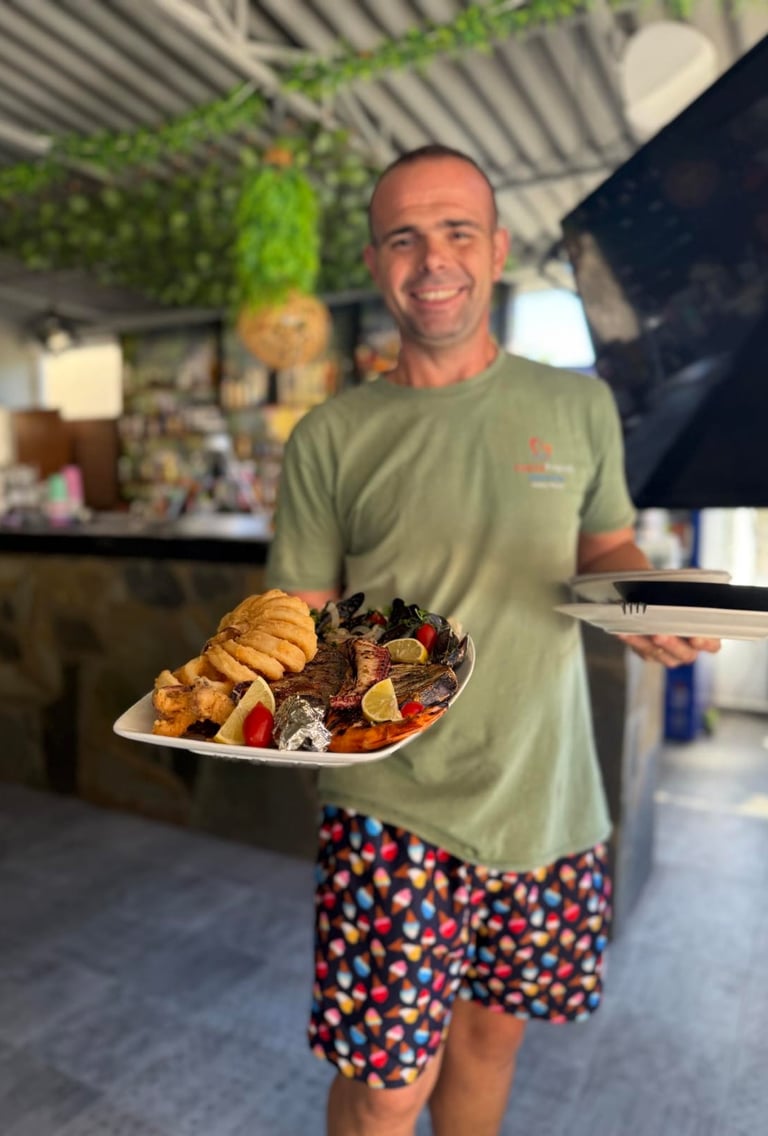 A smiling server holding a large platter of fresh Mediterranean grilled seafood and fried calamari.
