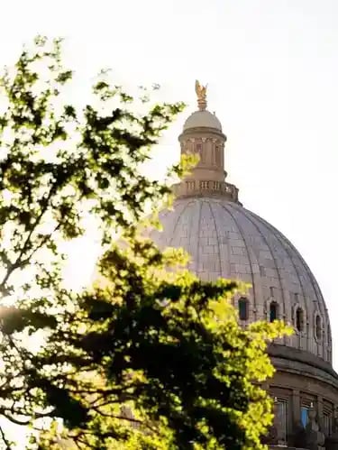 The Idaho State Capitol dome framed by green trees at sunset.