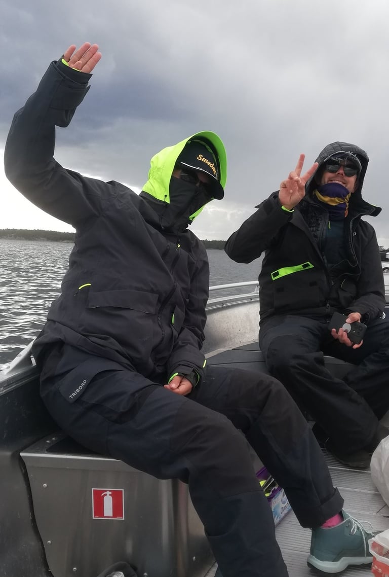 two people in black jackets and green pants sitting on a boat