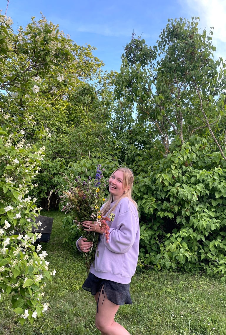 moteris apsirengusi violetiniu megztuku laiko gėles ir juokiasi