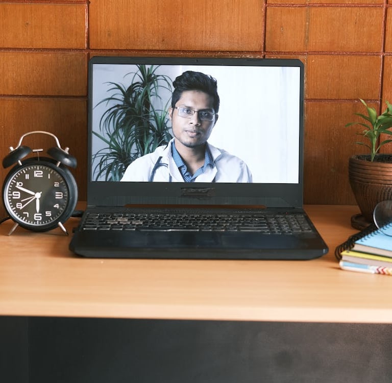 a laptop computer screen showing a doctor's face on a desk