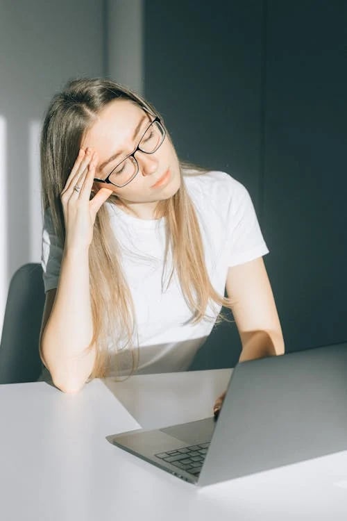 a woman in glasses and a white shirt is sitting at a table with a laptop