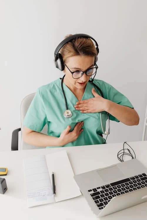 a nurse in a green scrubsuit is holding her hands on her chest