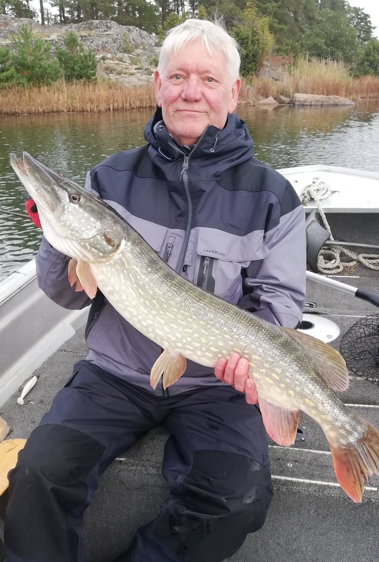 un homme est assis dans un bateau de pêche en suède, il a un beau brochet.
