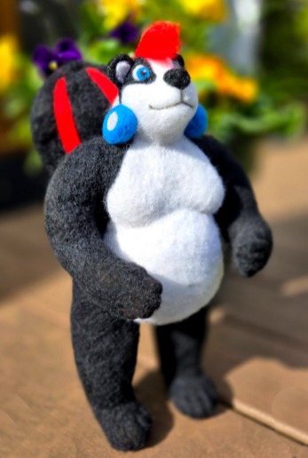 Handmade needle felted skunk figurine with a red mohawk and blue earrings standing outdoors.