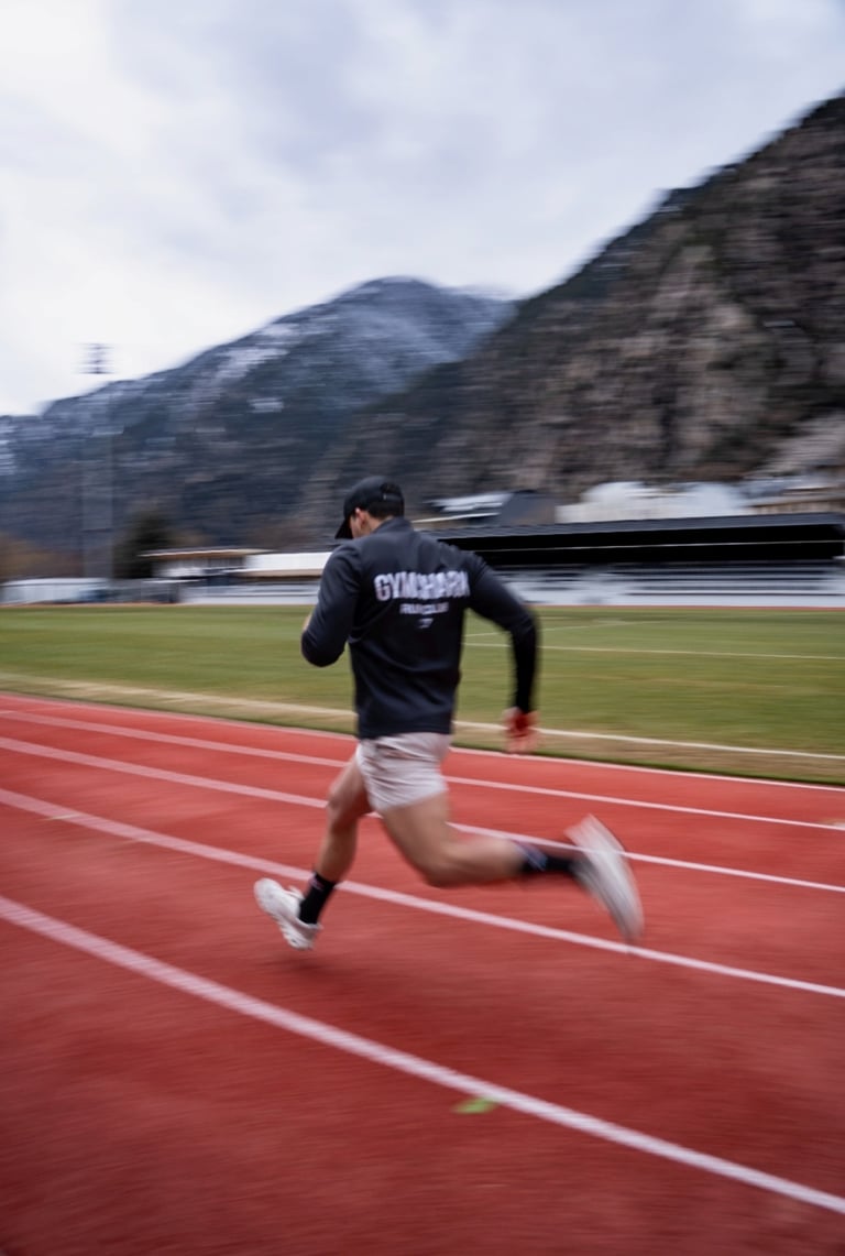 Male athlete in Gymshark apparel sprinting on a red outdoor track with mountains in the background.