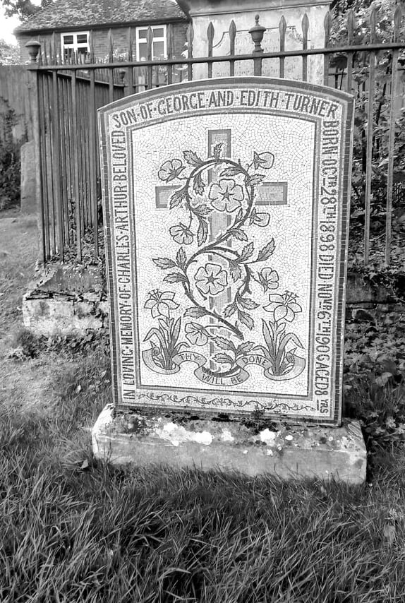 Vintage black and white mosaic gravestone in a cemetery with floral designs and a cross.