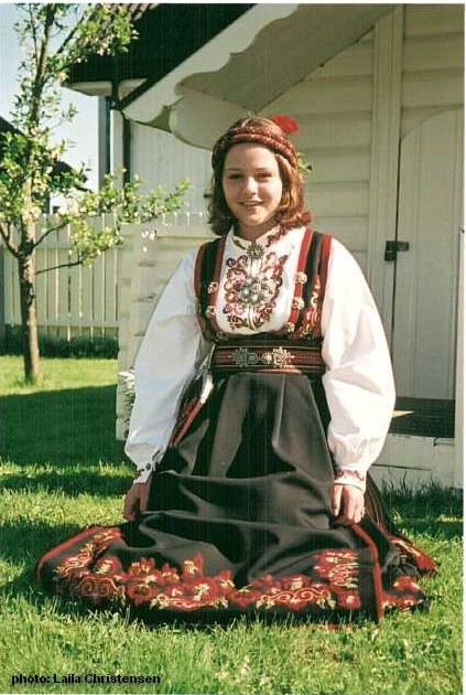 A girl sits in the grass wearing a bunad and head piece