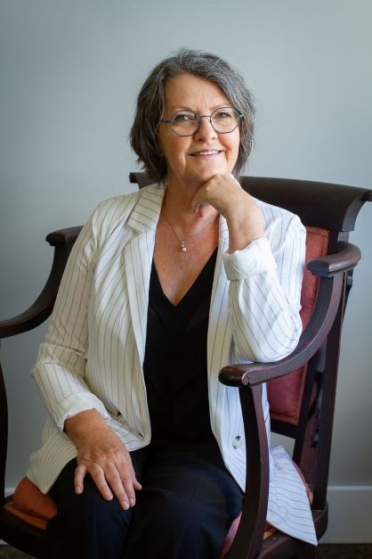  Joëlle Dechamplain assise, souriante, en veston rayé, incarnant l’accompagnement humain du deuil. 