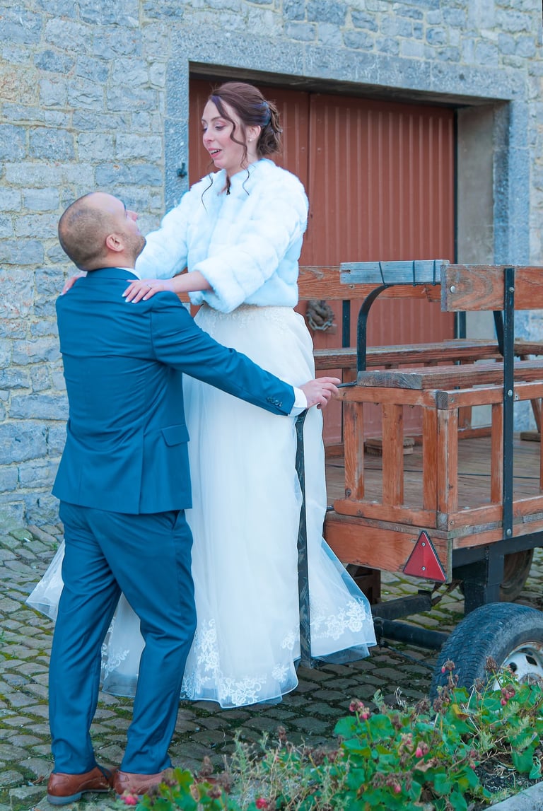 Un marié en costume bleu aide une mariée en robe blanche à descendre d'une calèche 
