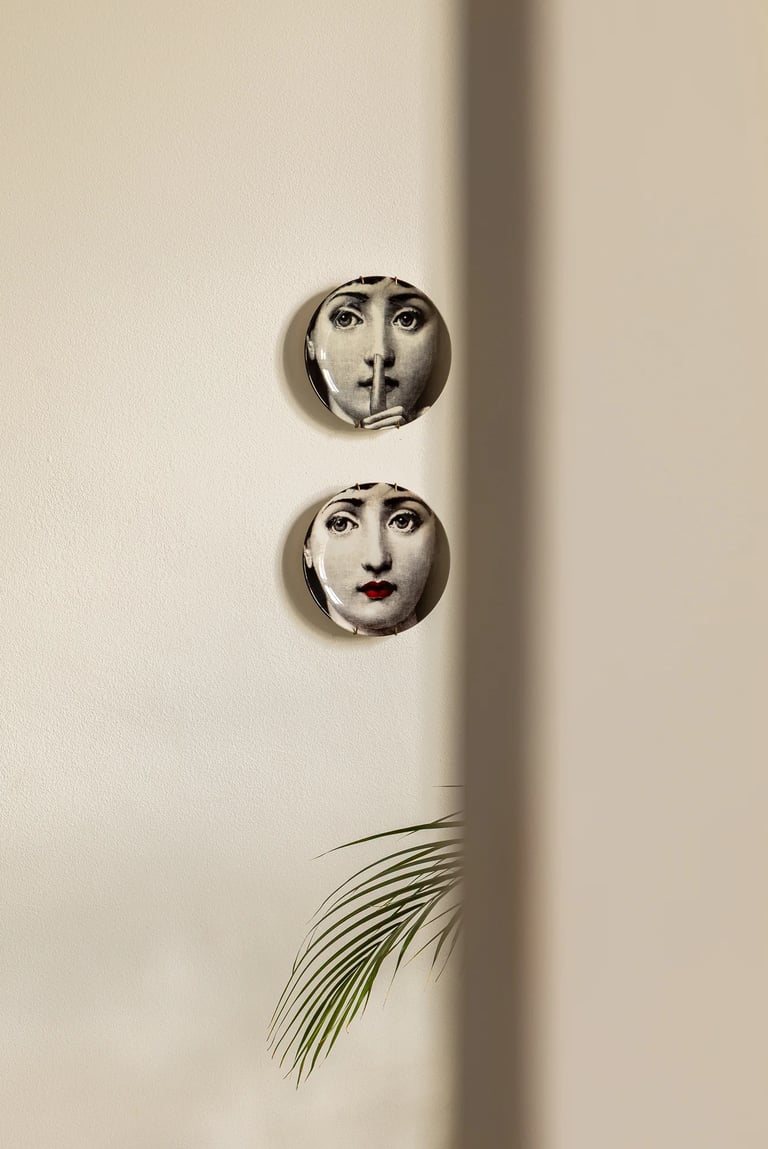 Ozdobne talerze Fornasetti na ścianie i gra światła.