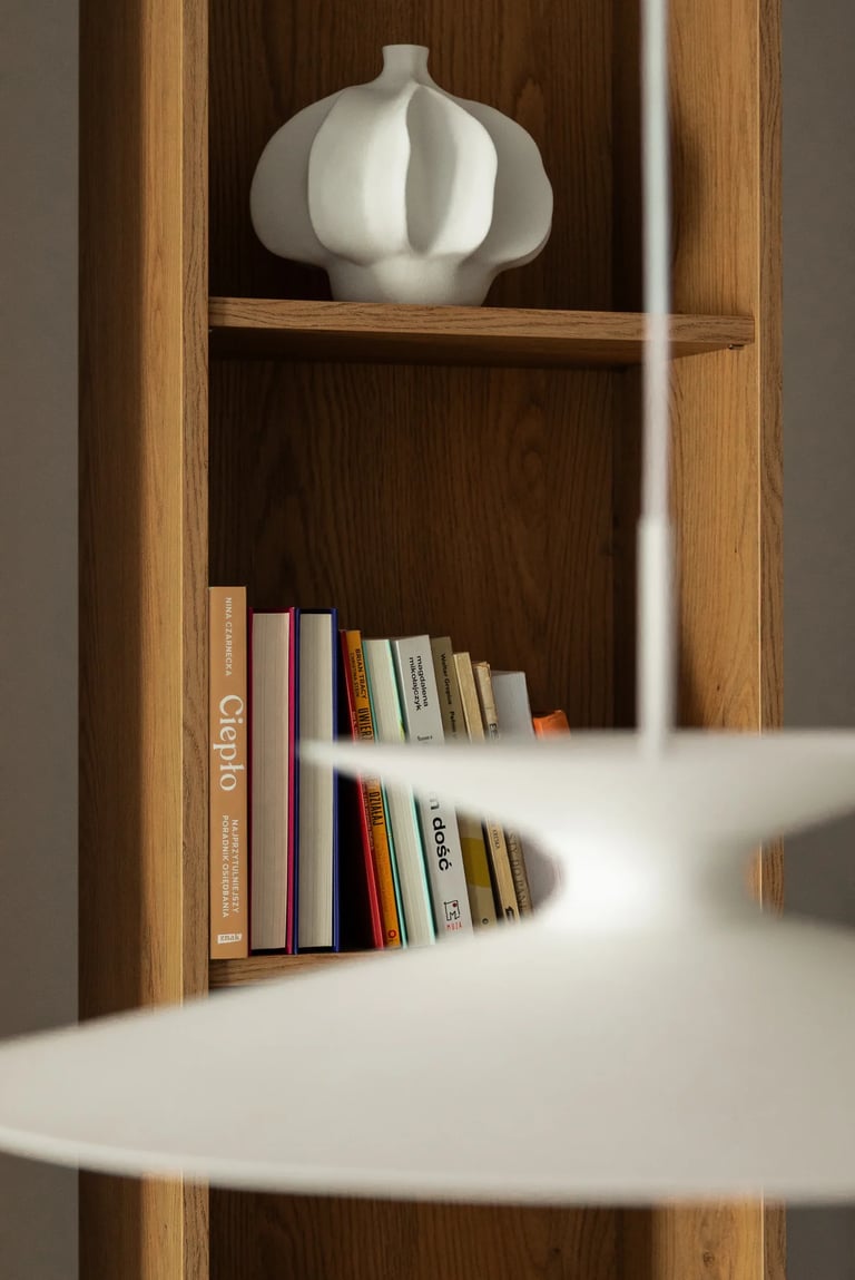 Drewniany regał z książkami i białym wazonem ceramicznym.