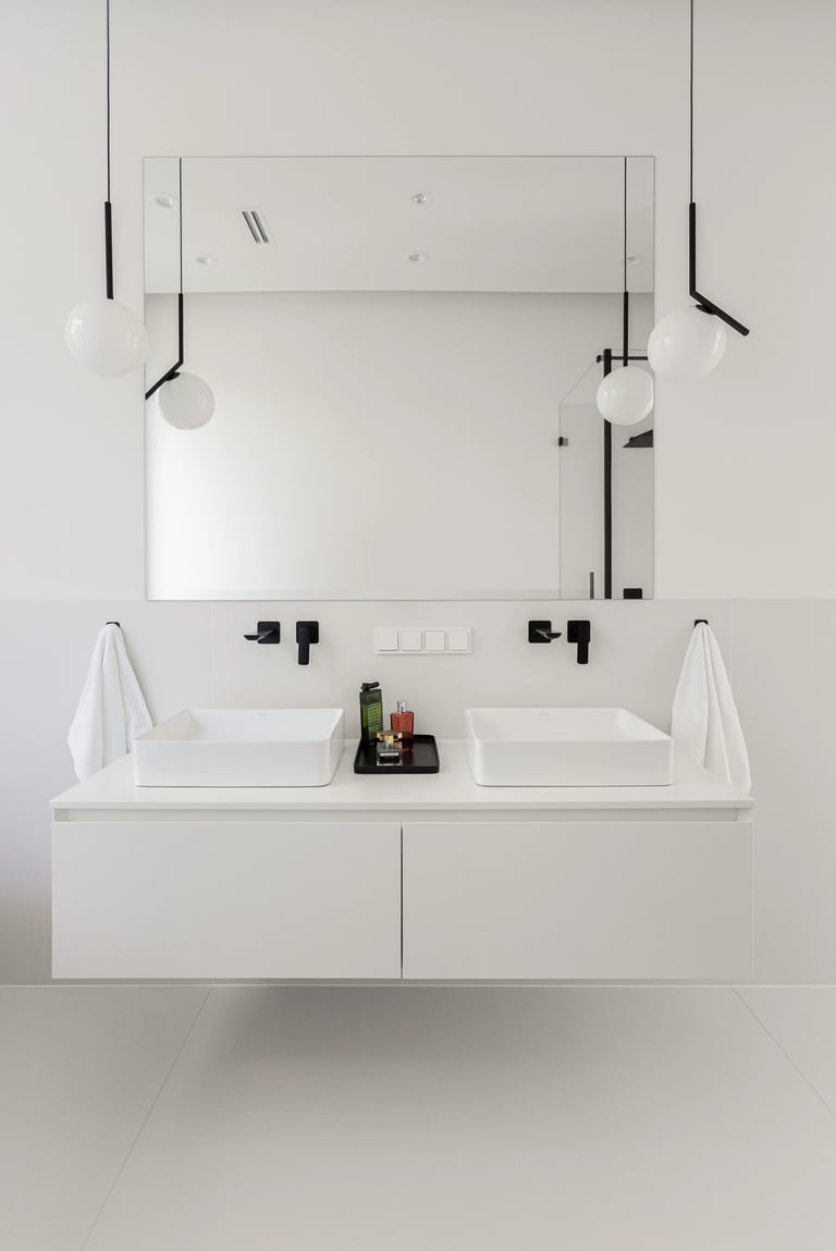 Minimalistyczna biała łazienka, szafka z dwema umywalkami, duże lustro i czarna armatura podtynkowa.