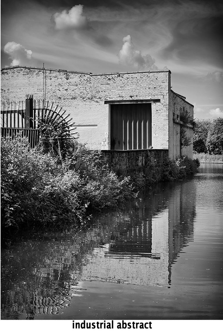 a black and white abstract photo of a mill with reflections in the canal