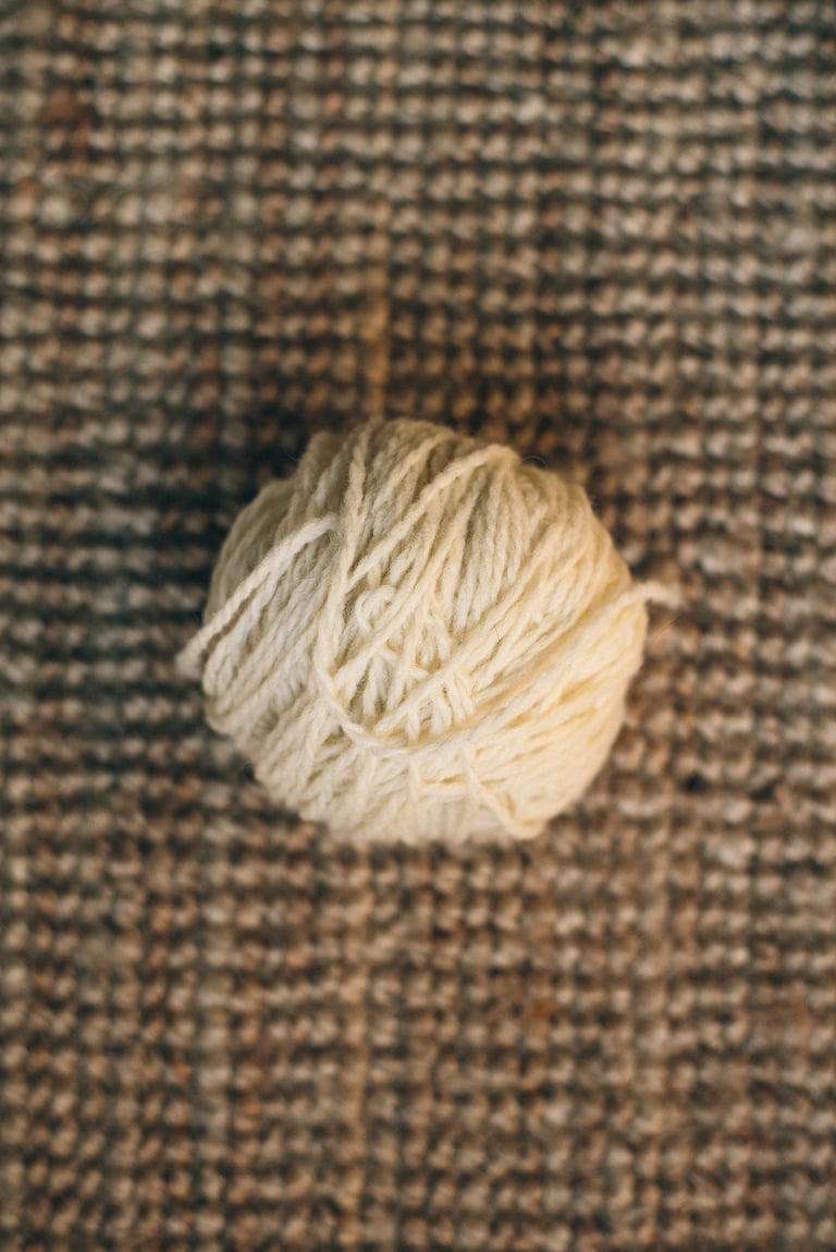 Nature morte d'une pelote de laine de pays écrue sur un fond de jute.