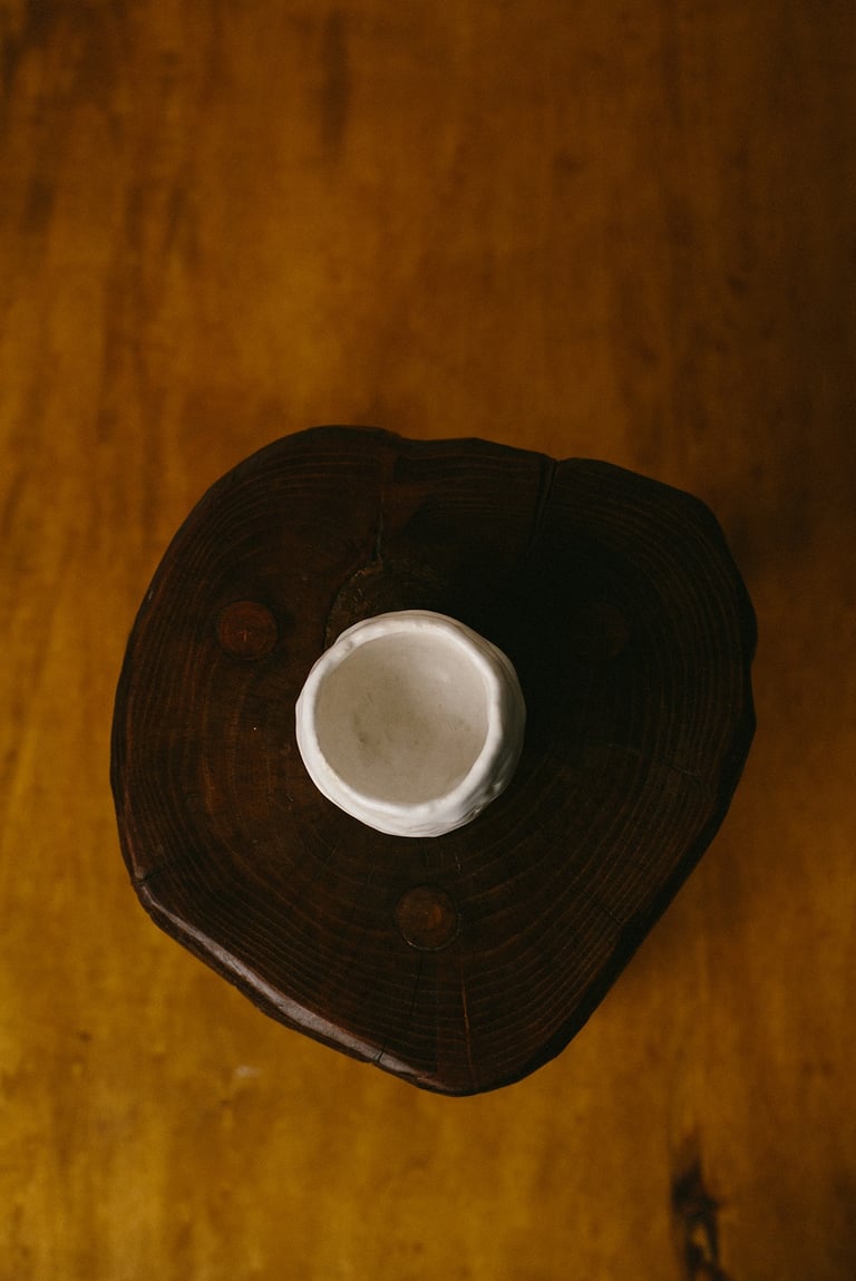 Vue plongeante sur un yunomi en grès blanc posé sur un tabouret en bois