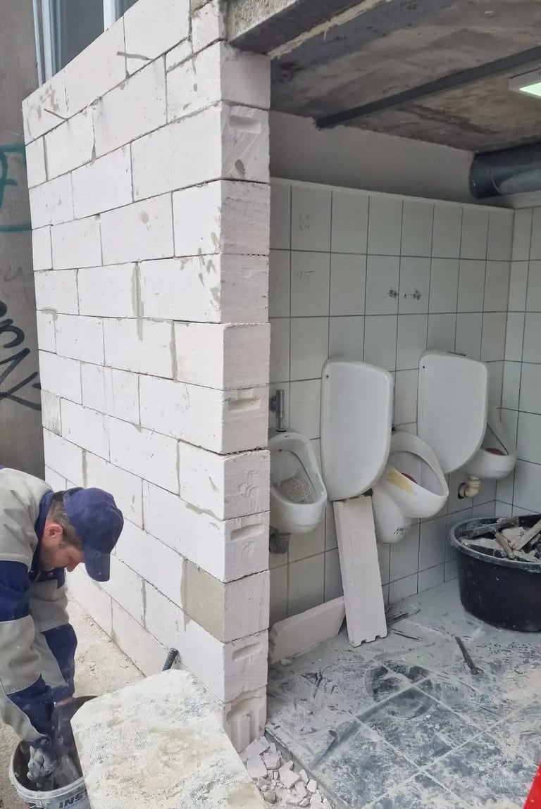A construction worker builds an aerated concrete block wall during a public restroom renovation.