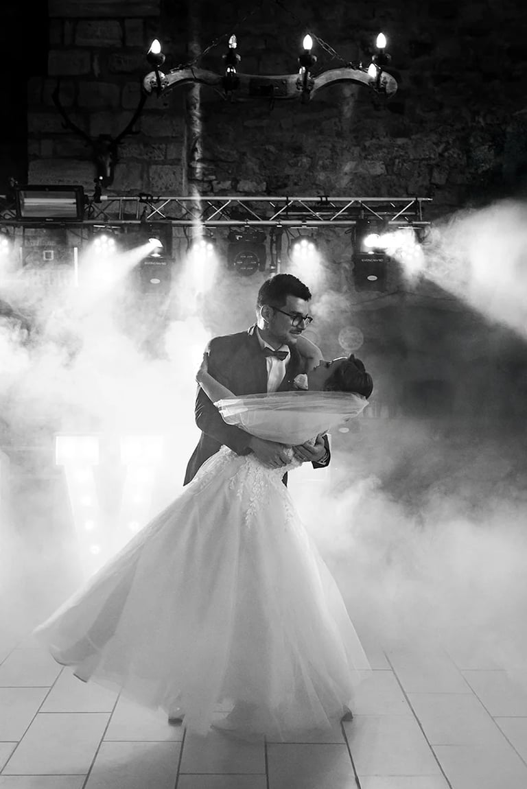 Marié portant sa femme dans ses bras lors de leur ouverture de bal, entourés de fumée et lumières.