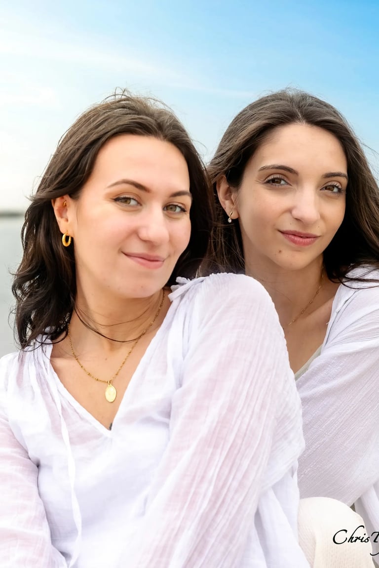 Portrait de deux soeur souriantes portant des hauts blancs légers, posant en extérieur devant la mer
