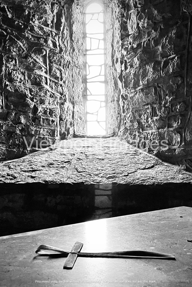 Black and white photo of a small stone cross on an altar inside a medieval castle window.