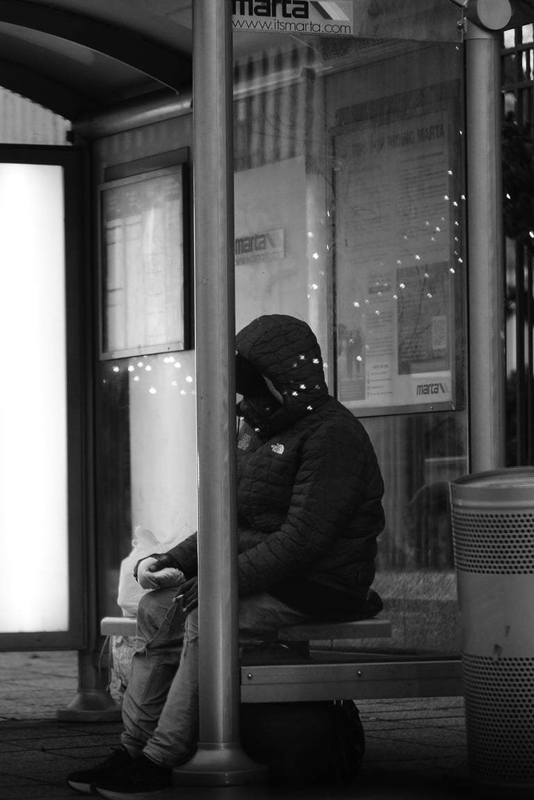 A person in a hooded puffer jacket sits at a black and white MARTA bus stop at night.