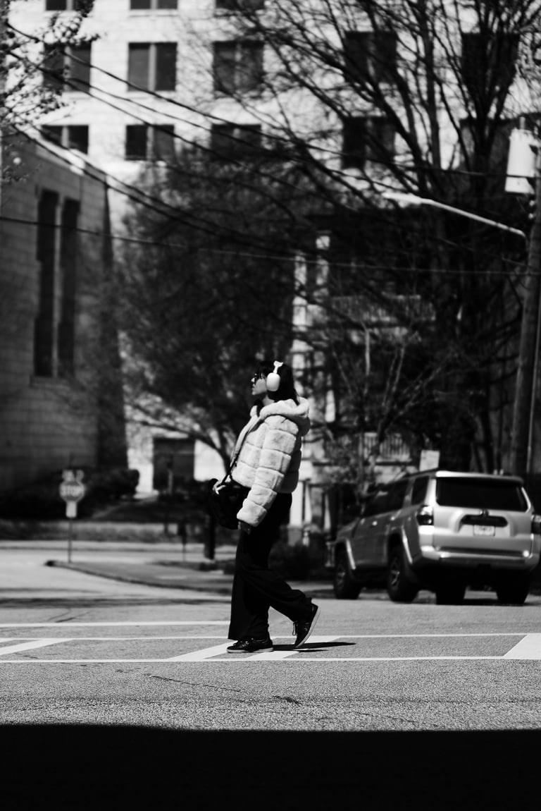 Black and white street photography of a person with headphones walking across a city crosswalk.