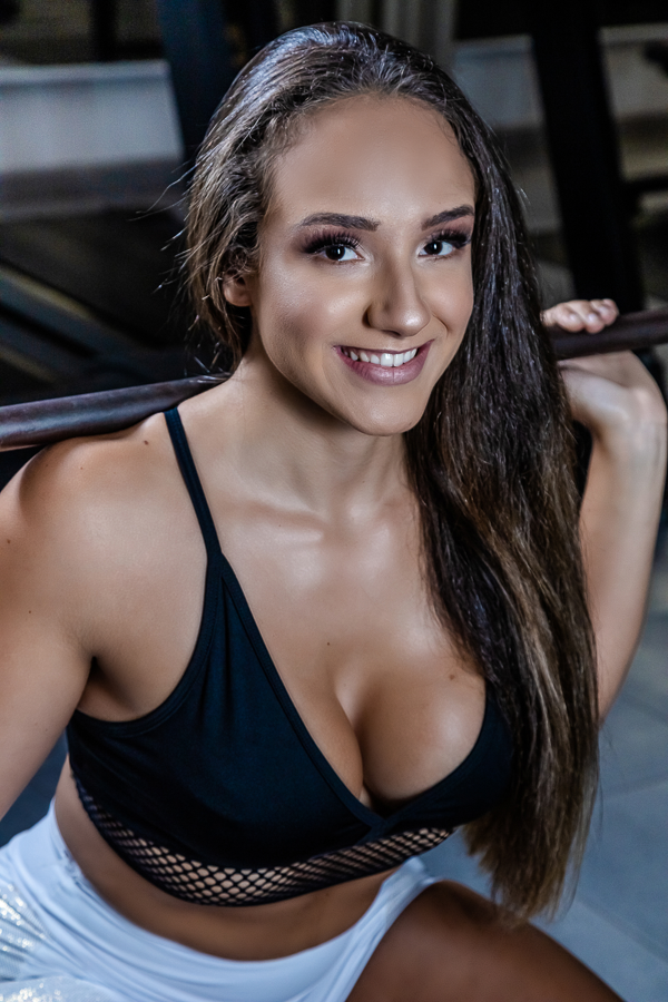 Mulher com cabelos longos usando top preto treinando agachamento com barra sorrindo