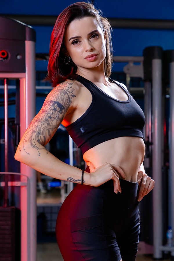 mulher na academia com mãos na cintura fundo colorido