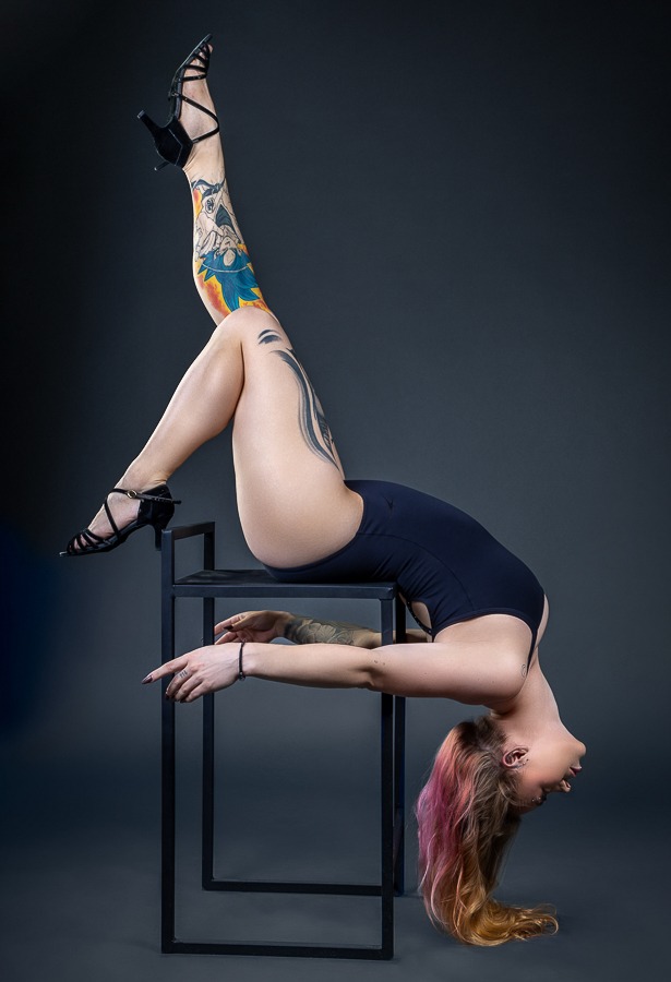 ginasta em pose artística com perna tatuada esticada e cabelos loiros jogados em fundo cinza