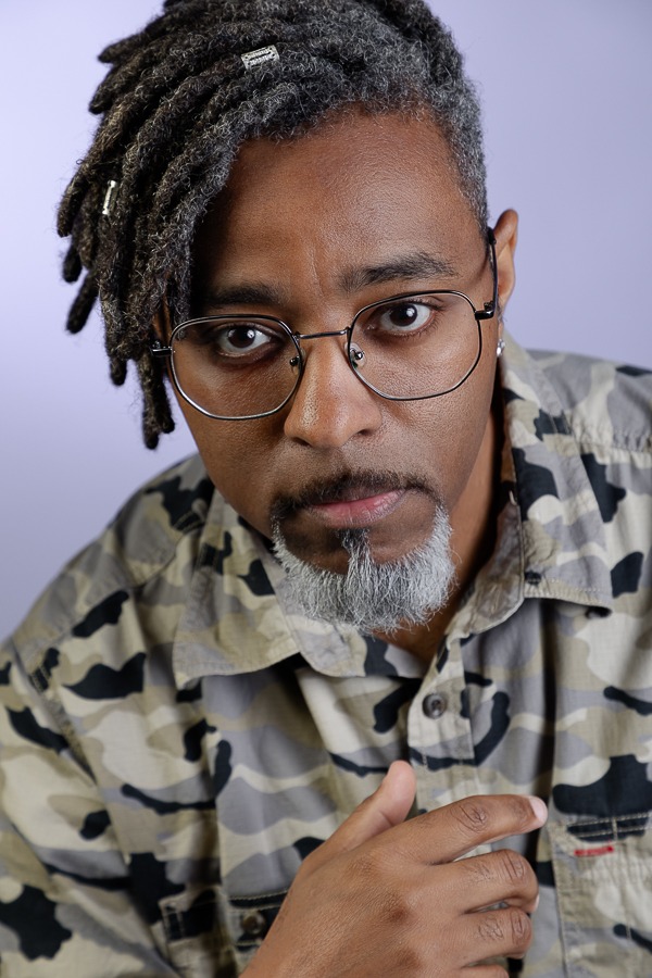 homem preto com camisa camuflada olhando diretamente pra frente em tom confiante