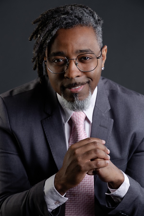 advogado moderno com dreads e barba sorrindo juntando as mãos vestindo terno cinza