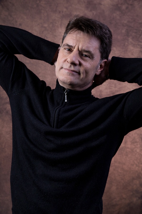 ator vestindo camisa preta em pose despojada cruzando os braços em ensaio fotográfico