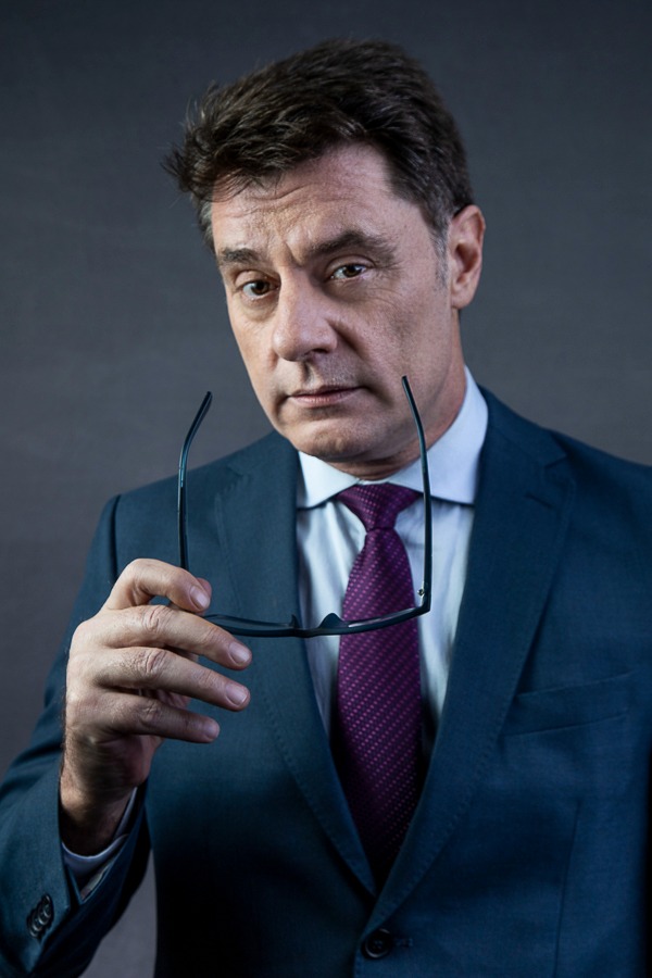 empresário de terno segurando óculos com olhar marcante em estúdio fundo cinza