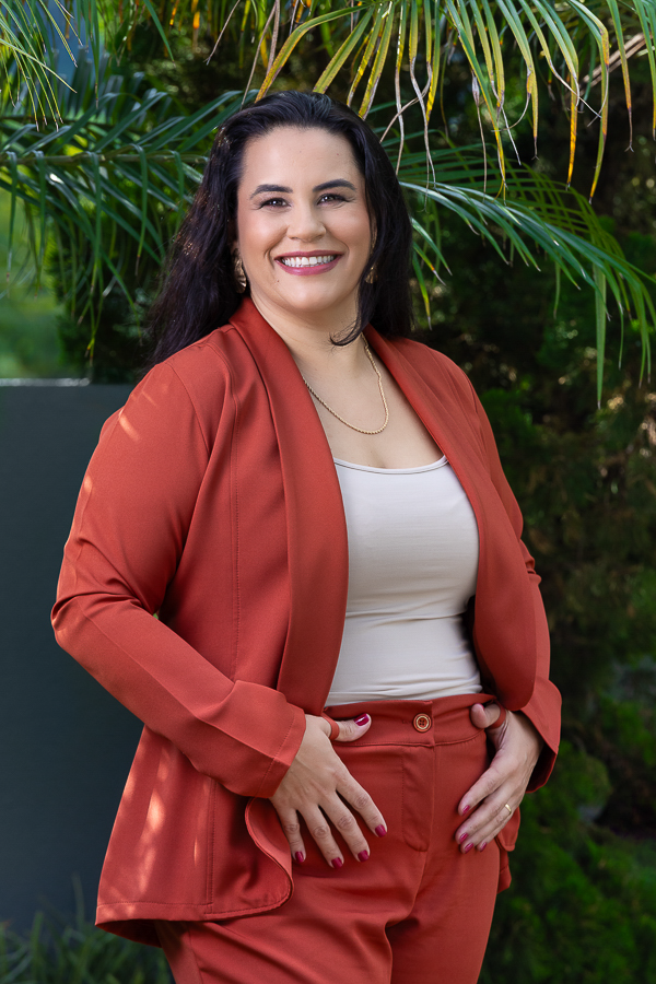 Mulher sorrindo, cabelos escuros , vestindo conjunto terracota, posando no jardim
