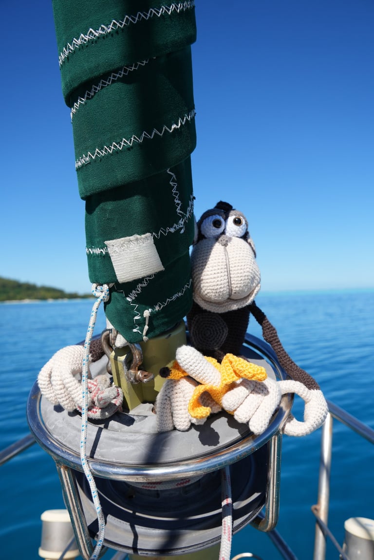 A cute crochet chimpanzee sitting on a sailboat mast with a banana on a sunny day at sea.