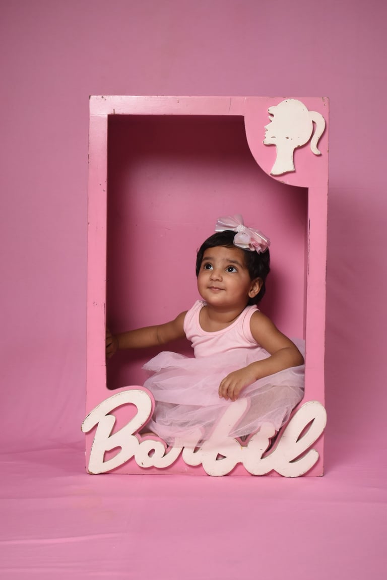 Baby girl in a pink tutu posing inside a Barbie-themed toy box for a creative photoshoot. Wonderpose
