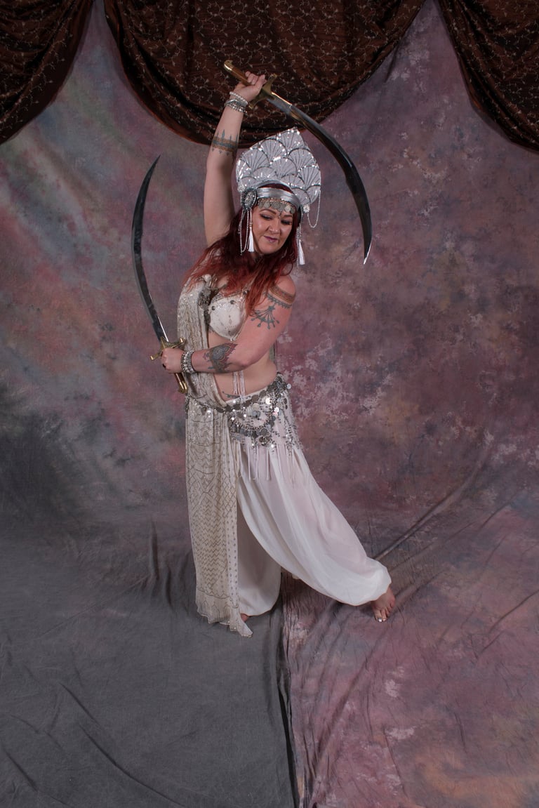 Bellydancer Shahravar with double swords wearing white assuit costume with coin bedlah