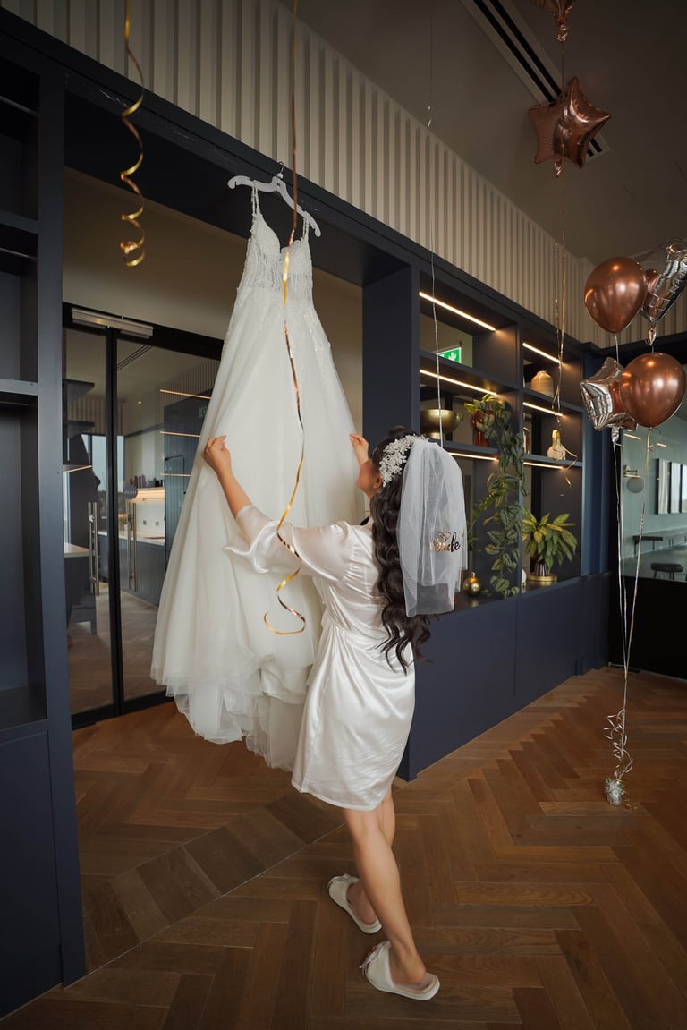 Bride in a silk robe reaching for her wedding dress before the ceremony, captured by Fred Art Studio