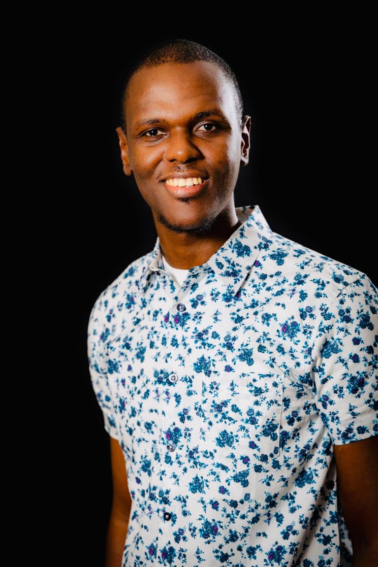 Portrait of a smiling young Black man in a stylish white and blue floral short-sleeved shirt.