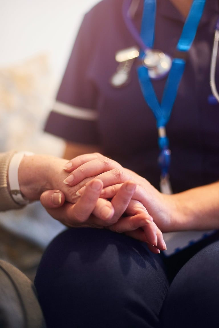 A healthcare nurse in blue scrubs holding an elderly patient's hand to provide comfort and support.