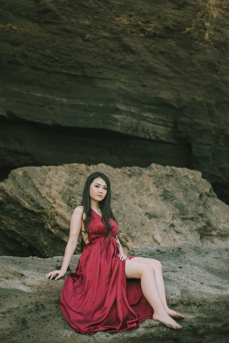 Intimate female portrait in red dress on the rocks during sunset at Pantai Nyanyi Bali.
