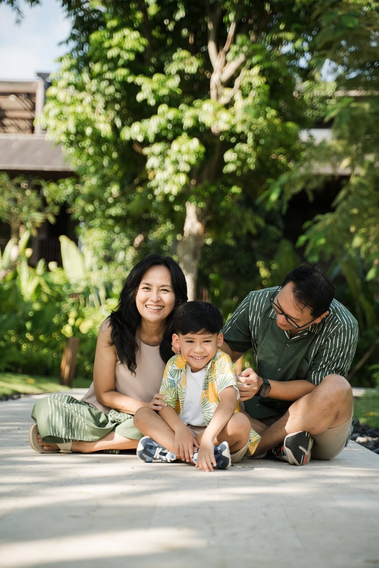 Parents sitting with their child on a garden pathway during a family photography session at The Meru Sanur Bali
