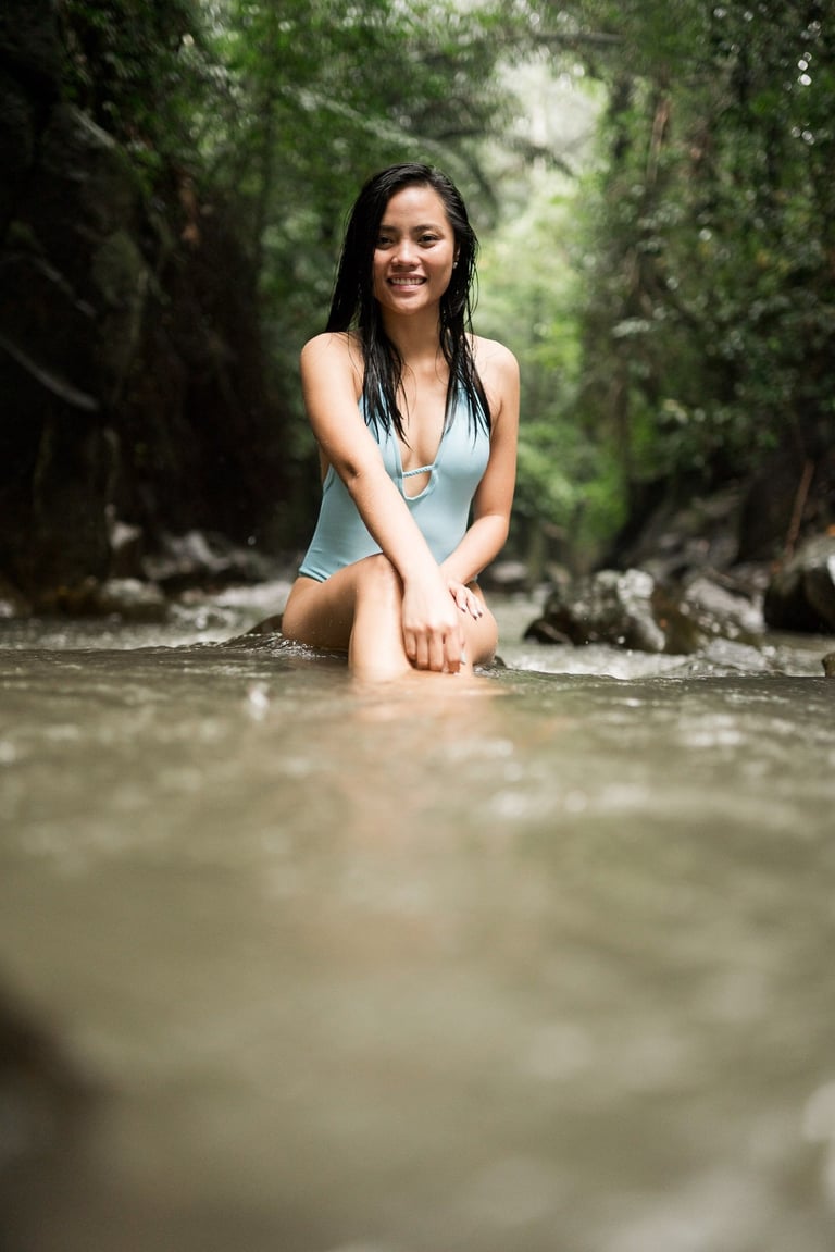 Woman sitting in shallow water during portrait session at Kanto Lampo Waterfall Bali