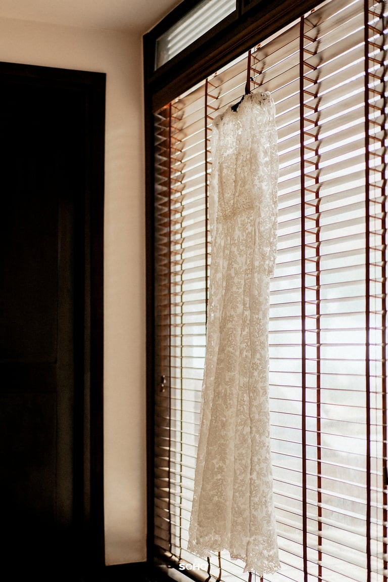 a wedding dress hanging in a window with a dress hanging from a window