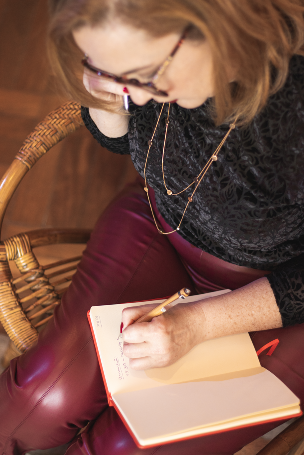 A professional woman in red leather pants writes in a notebook while talking on her phone.