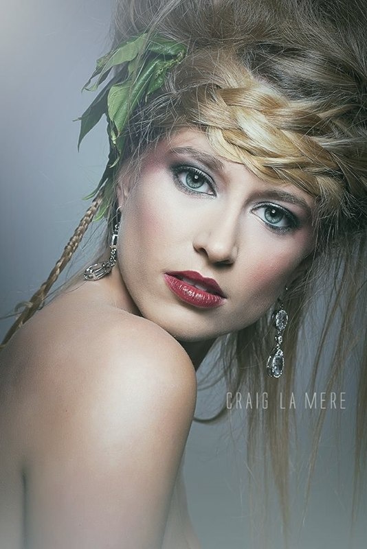 Woman with avant garde braided hairstyle with green leaves, bold red lipstick, dramatic eye makeup and statement earrings.