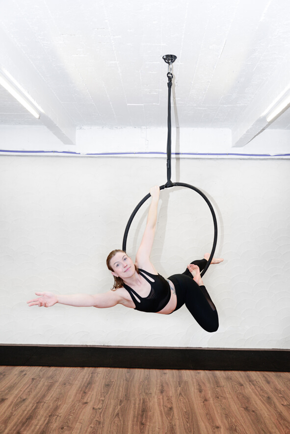 Vrouw in zwarte outfit voert een aerial hoop oefening uit bij De Polecats Fabriek in Gent