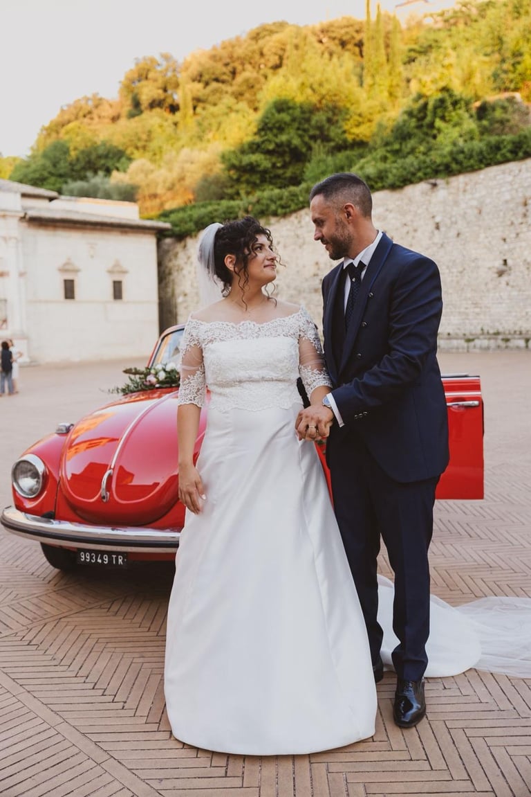 Sposi che si guardano innamorati in una suggestiva piazza con il maggiolone sullo sfondo.